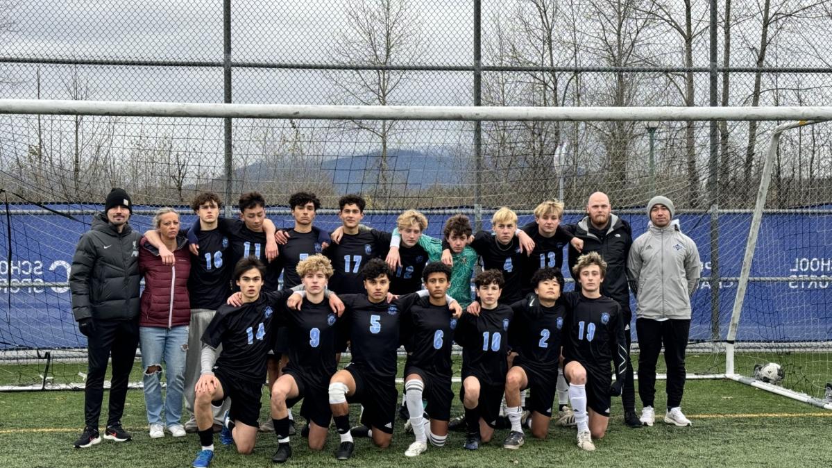 A youth boys' soccer team poses in dark team kit on a soccer pitch in front of a net.