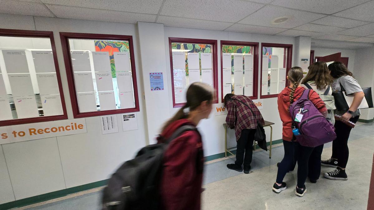 High school students gather at a table in front of a wall adorned with action post-its