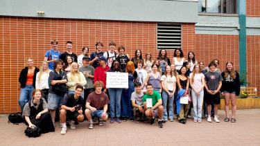A group of high school students posing in front of their brick high school