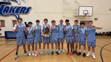 A high school boys sports team in light blue shorts and shirts poses in a school gymnasium