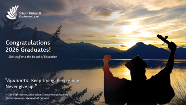 Silhouette of a person in cap and gown with arms raised holding a diploma, in front of a lake and mountains at sunset