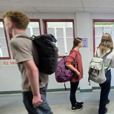 Students walk through a hallway with windows covered in white paper on one side.